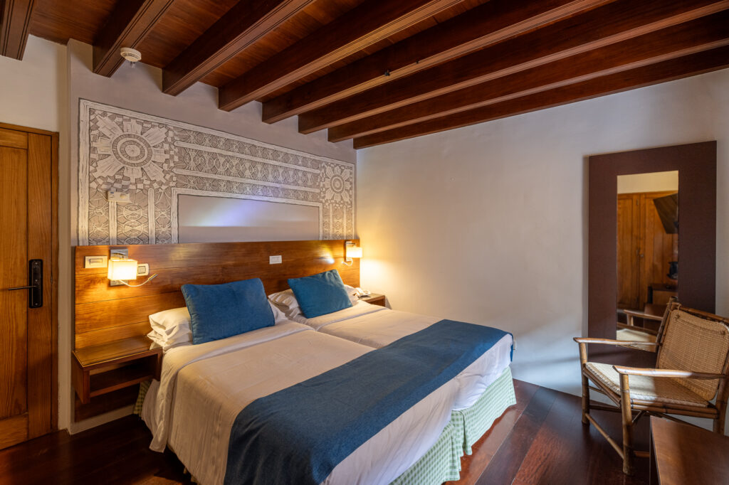 Interior de una de las habitaciones del hotel La Quinta Roja decorada con un mural que muestra un tipo de calado canario